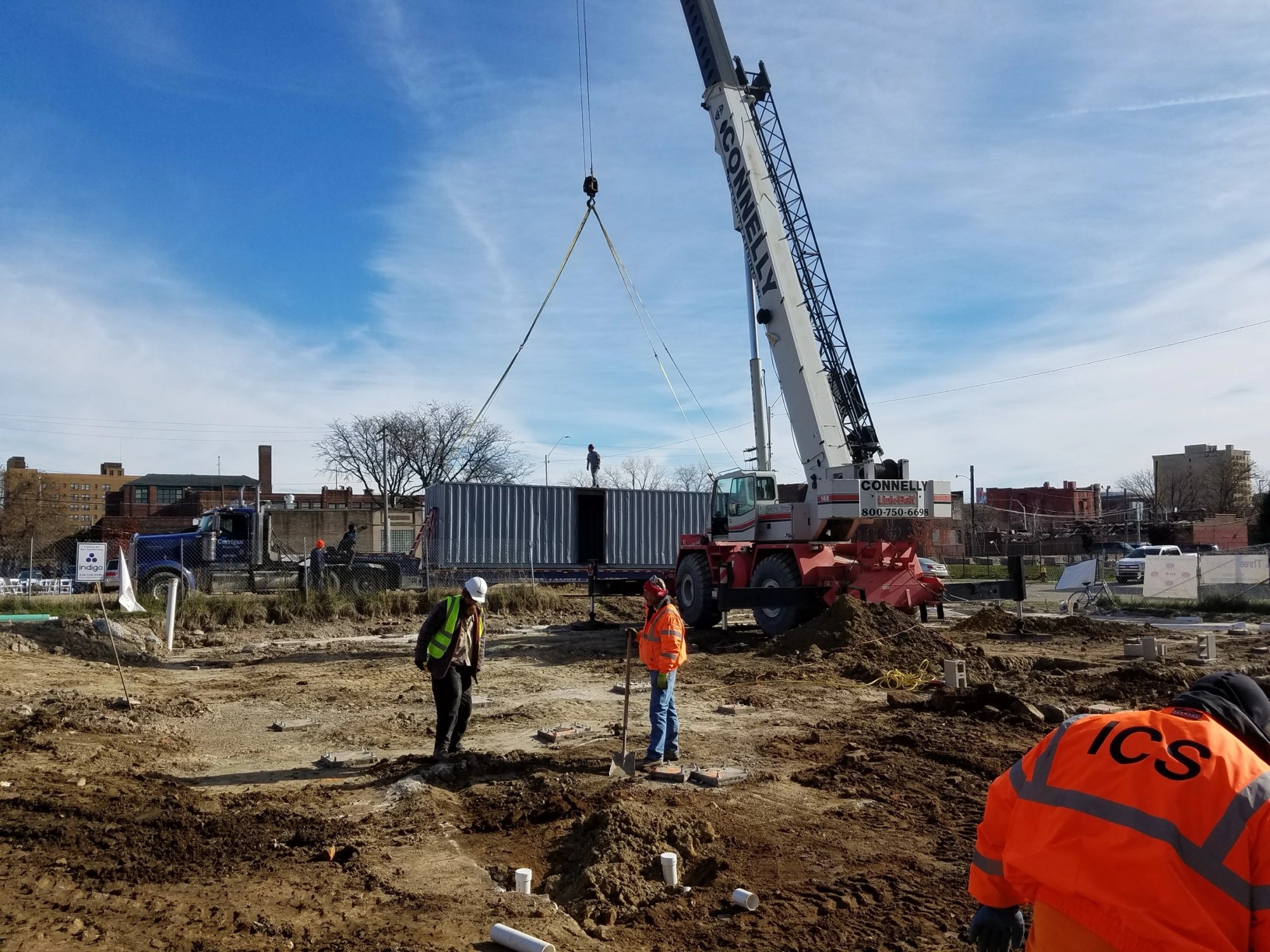 An ICS jobsite with a crane and crew working a cleared multi-phase construction site under a clear sky
